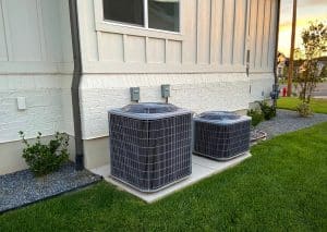Two outdoor central air conditioning units installed on concrete pads beside a residential home, surrounded by a neatly maintained lawn and landscaping.